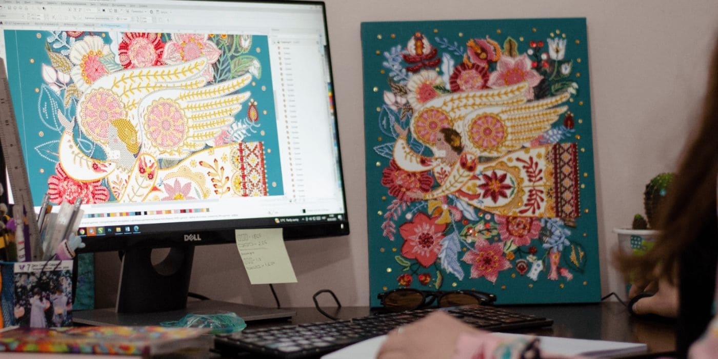 An Abris Art designer working on an embroidery chart on screen next to the finished piece